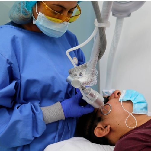 Profesional médico aplicando tratamiento láser facial a paciente para eliminar cicatrices.